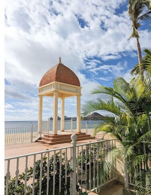 Ein Pavillon mit Kuppel, nahe einem Strand mit blauem Himmel und Palmen.