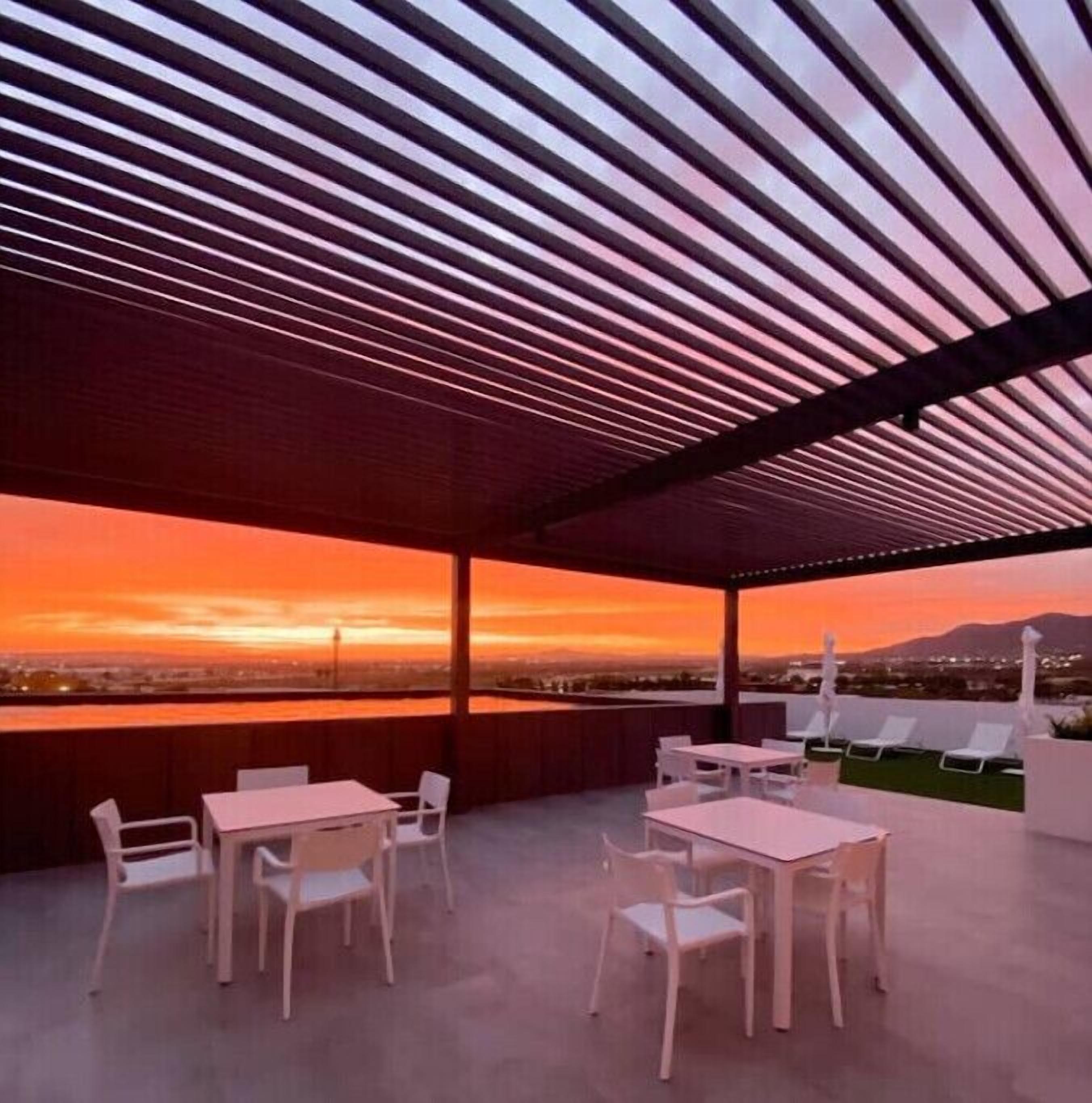 An outdoor seating area with tables and chairs, overlooking a sunset view.