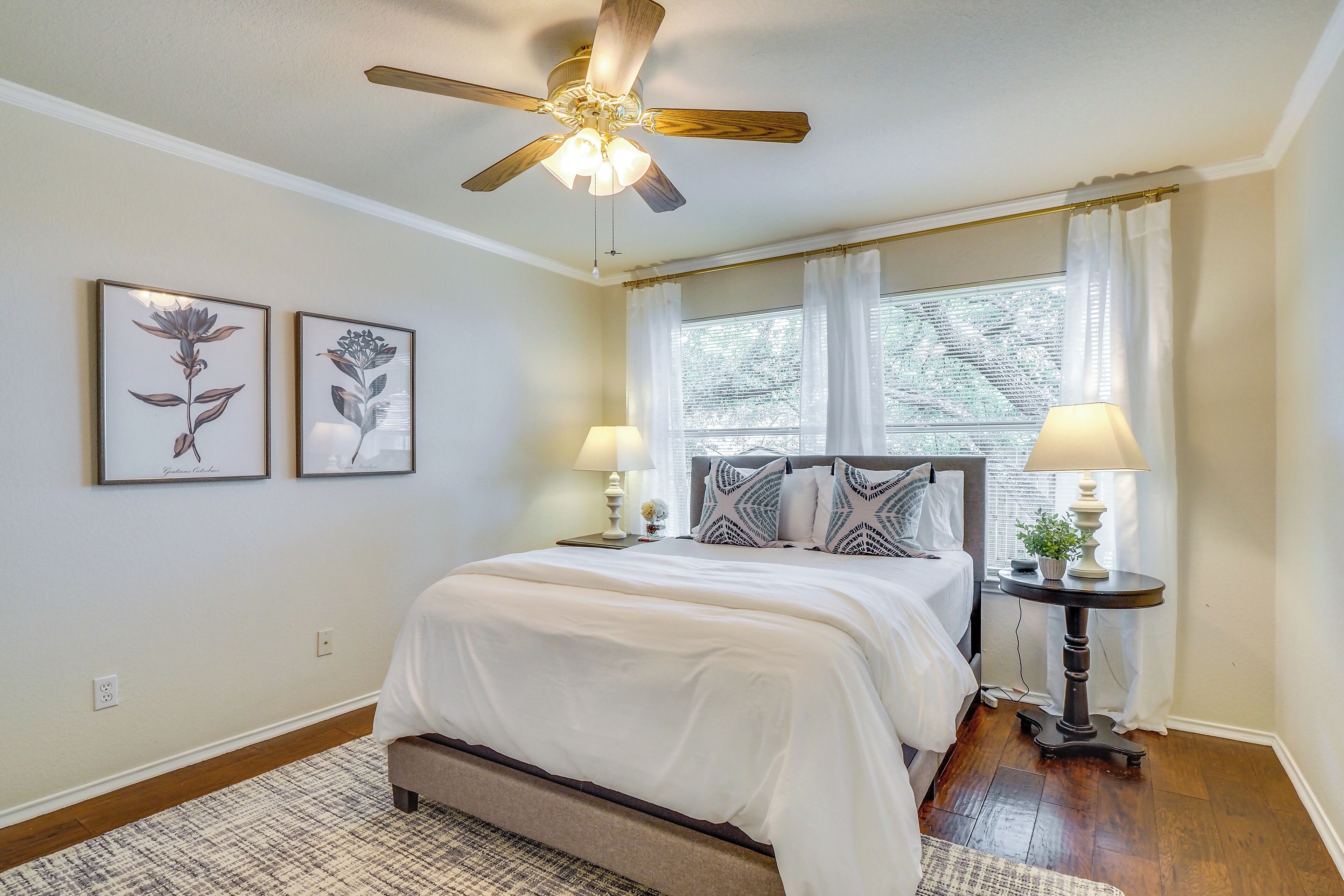 A bedroom with a bed, two bedside tables, a ceiling fan, and a window with curtains.