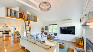Ein geräumiges Wohnzimmer mit Holzboden, einem weißen Sofa, einem Couchtisch und einem Kamin.