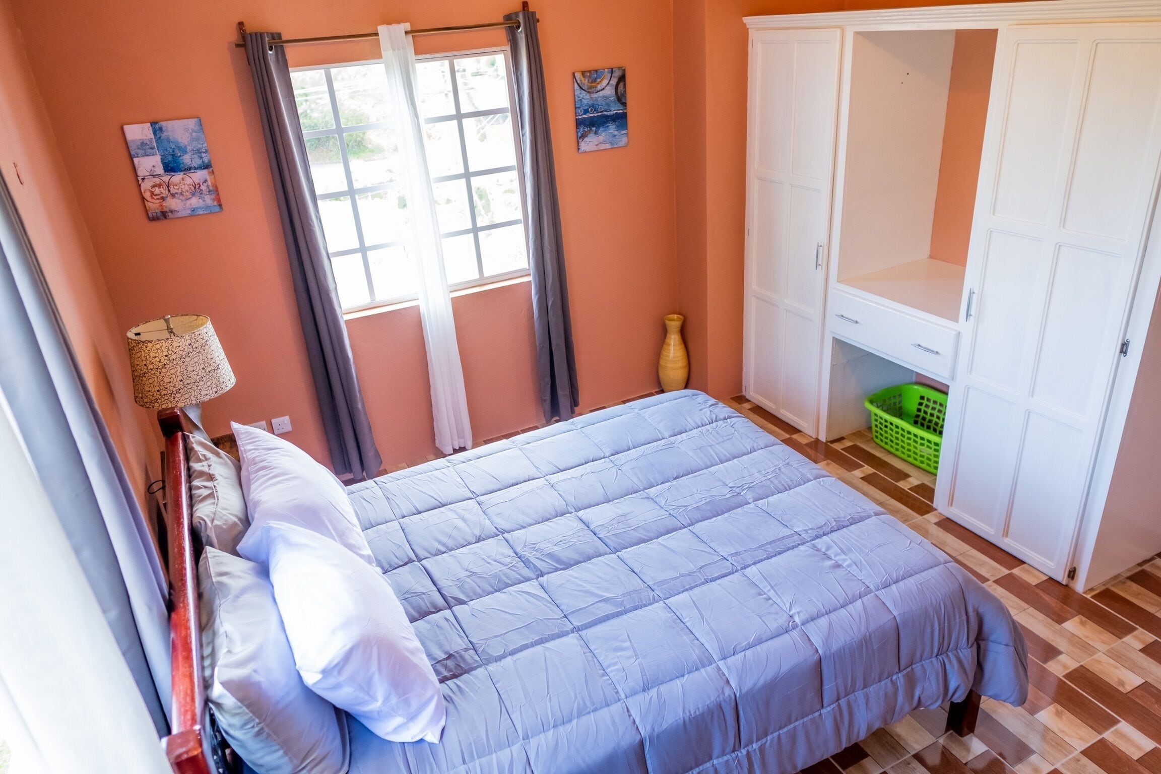 Een slaapkamer met een bed, een kledingkast, een raam met gordijnen en een vaas op de vloer.