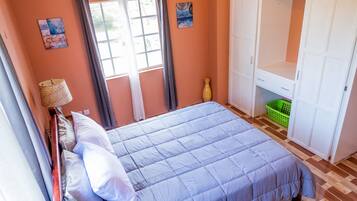 Een slaapkamer met een bed, een kledingkast, een raam met gordijnen en een vaas op de vloer.