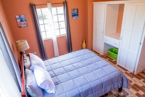 Une chambre à coucher avec un lit, une armoire, une fenêtre avec des rideaux et un vase posé sur le sol.