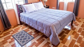 Una cama bien hecha con una colcha estampada, una lámpara de noche y una alfombra decorativa sobre un piso de madera.