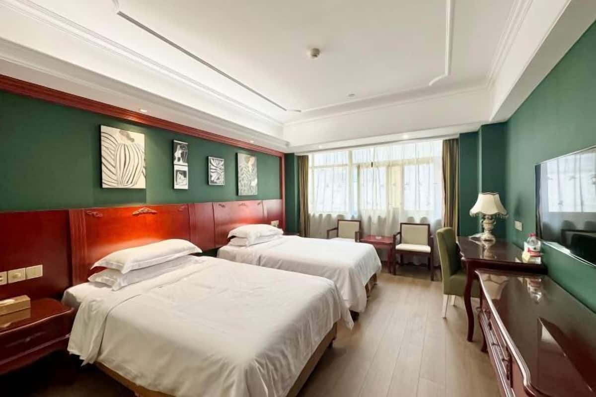 Une chambre d’hôtel avec deux lits, un bureau, une chaise et une grande fenêtre avec des rideaux.