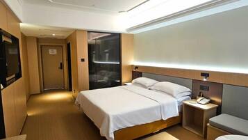 A hotel room with a bed, bedside table, and a small desk with a phone.