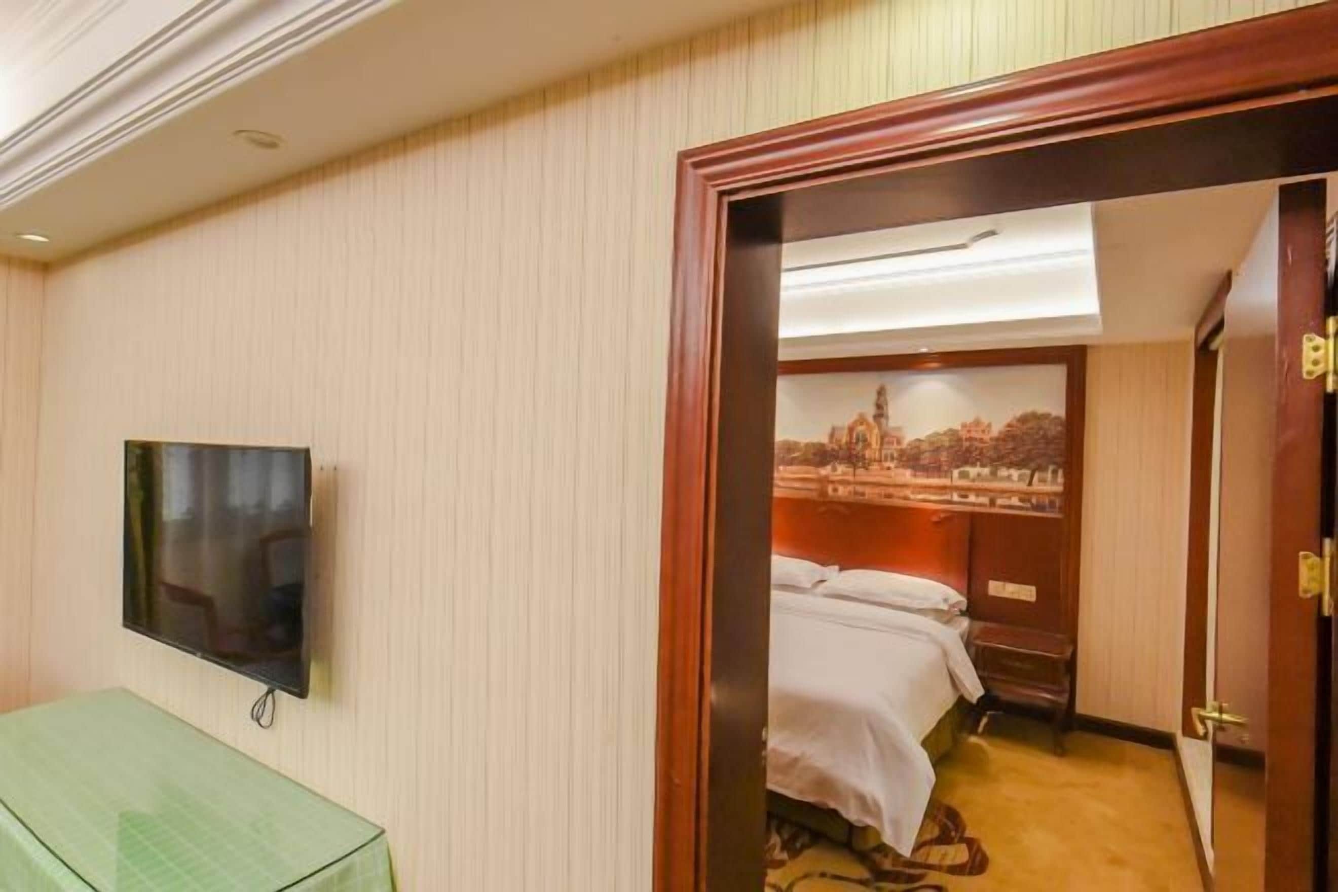 A hotel room with a bed, a television mounted on the wall, and a door leading to another room.