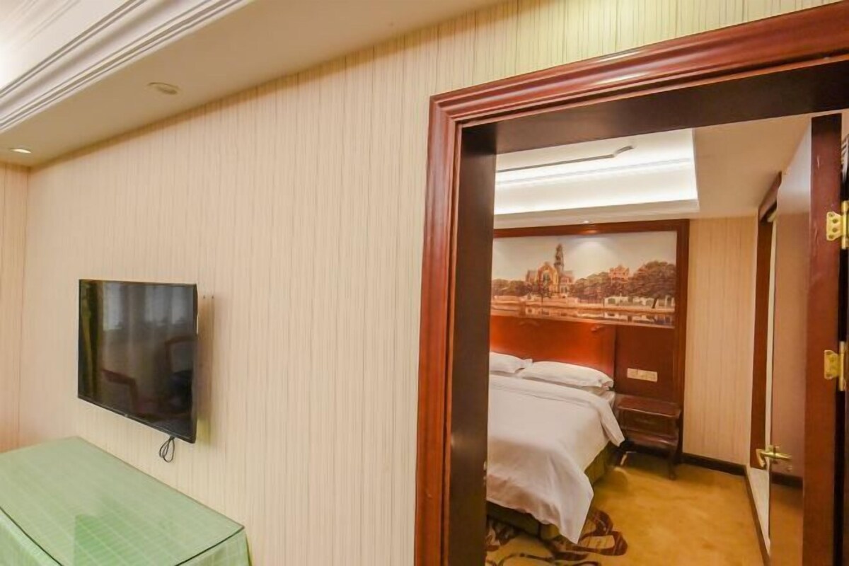 A hotel room with a bed, a television mounted on the wall, and a door leading to another room.