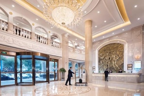 A spacious lobby with a grand chandelier, a reception desk, and a large decorative wall. - Fenghua Hotel (Ningbo)