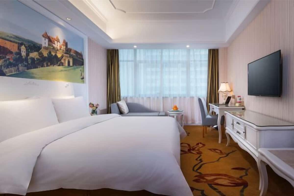 Une chambre d’hôtel avec un grand lit, un bureau, une télévision et un tableau au mur.