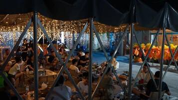 Un área de comedor al aire libre con mesas y sillas, rodeada por una estructura tipo carpa.
