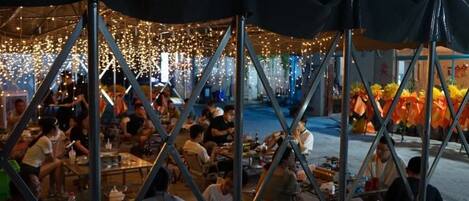 An outdoor dining area with tables and chairs, surrounded by a tent structure.