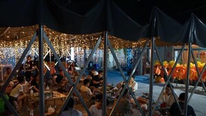 Een terras met tafels en stoelen onder een overkapping, omringd door veel mensen.