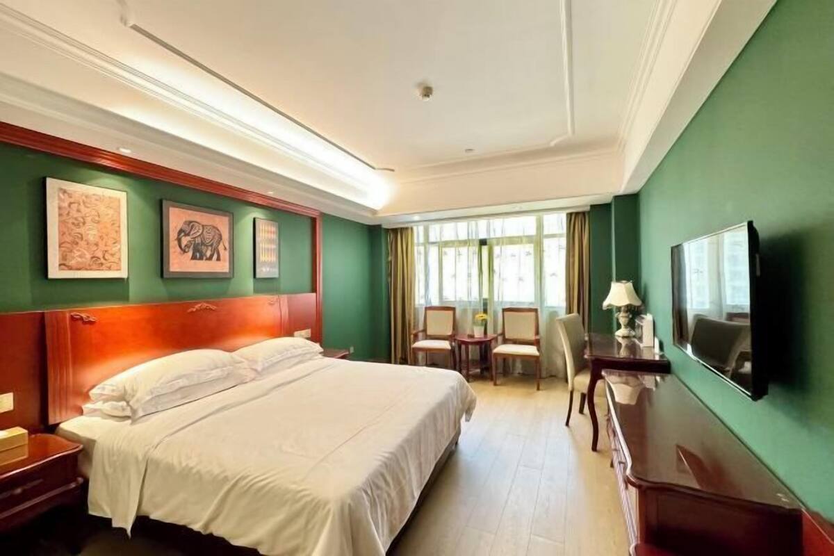 Une chambre d’hôtel avec un grand lit, un bureau, une chaise, une télévision et des œuvres d’art accrochées aux murs.