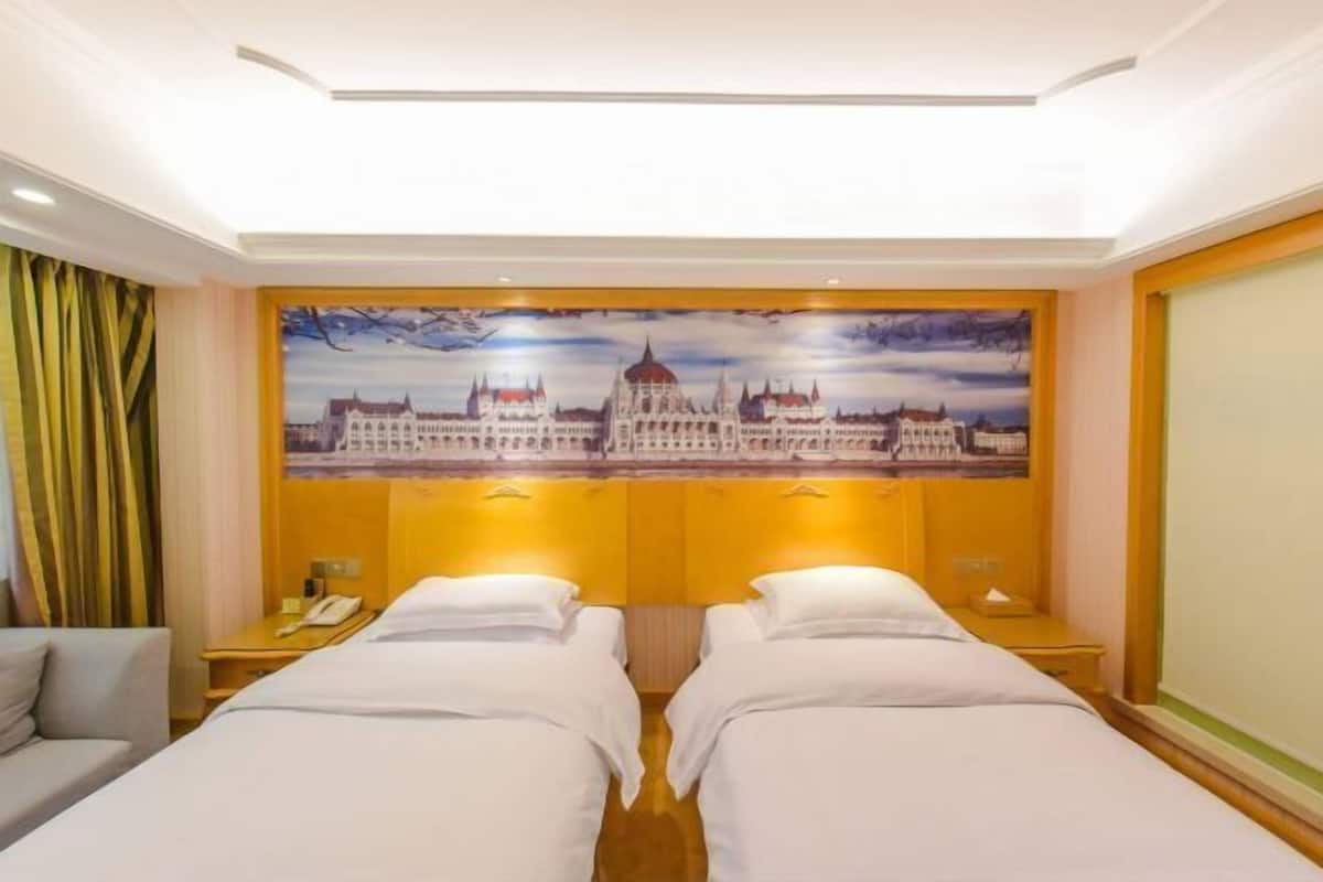 Une chambre d’hôtel avec deux lits, un tableau représentant un bâtiment, un téléphone et une table de chevet.