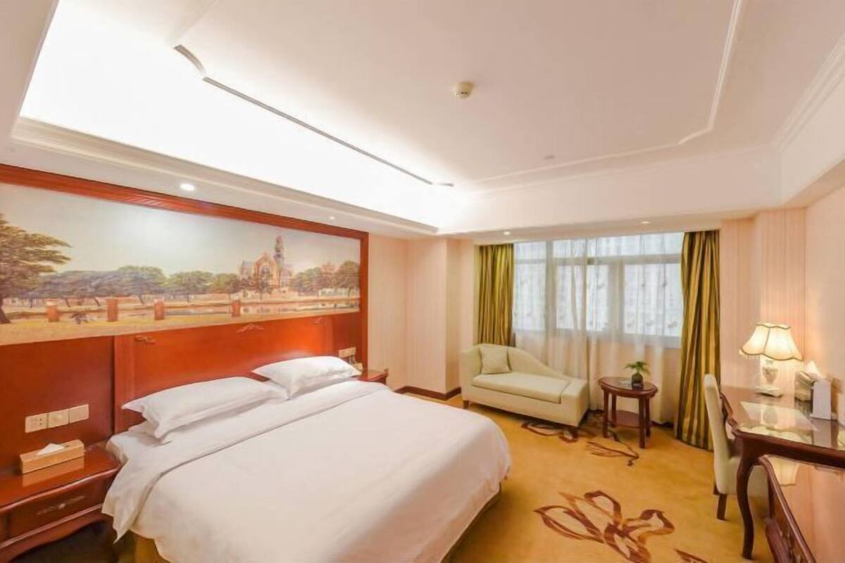 Une chambre d’hôtel avec un grand lit, un bureau avec une lampe, une chaise et un tableau au mur.