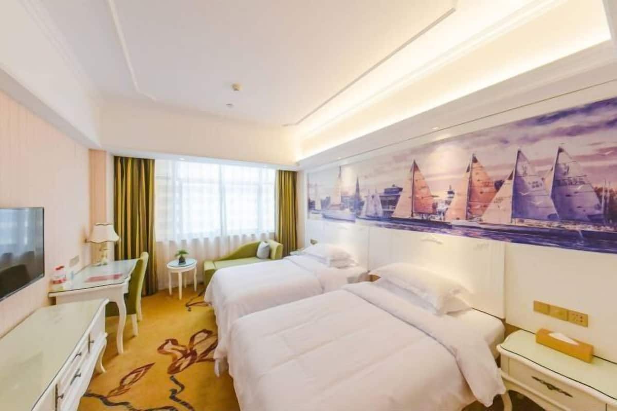 Une chambre d’hôtel avec deux lits, un bureau, une chaise, une télévision et une fenêtre avec des rideaux.
