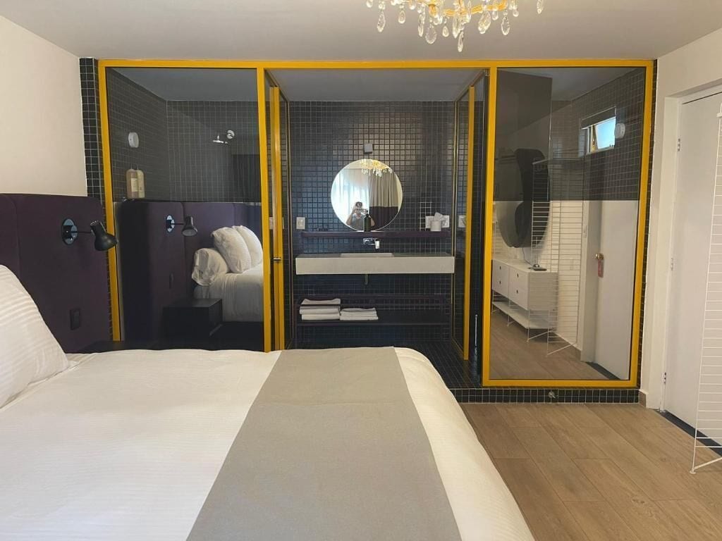 Een hotelkamer met een bed, een spiegel, een badkamer met douche en een televisie.