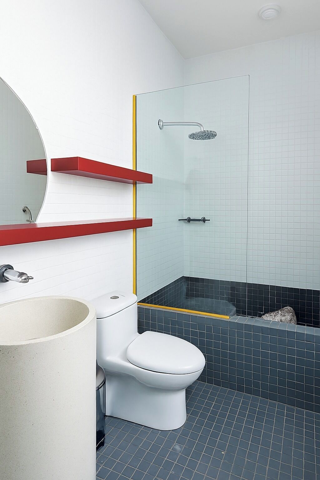 Un baño con inodoro blanco, lavamanos con encimera roja, cabina de ducha de cristal y suelo de baldosas.