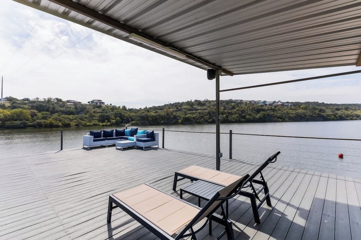 Une terrasse en bois avec mobilier d’extérieur, un espace abrité et une vue sur un lac et des collines.