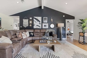 A modern living room with a sectional sofa, a coffee table, and a black accent wall with framed artwork. - Lakefront Paradise With Firepit (Marble Falls)