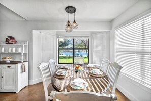 A dining area with a table set for six, white chairs, a window with blinds, and a view of the outdoors. - Lakefront Paradise With Firepit (Marble Falls)
