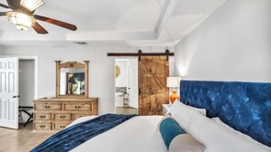 Ein Schlafzimmer mit Bett, Kommode, Spiegel, Deckenventilator und einer Schiebetür im Bauernhausstil.