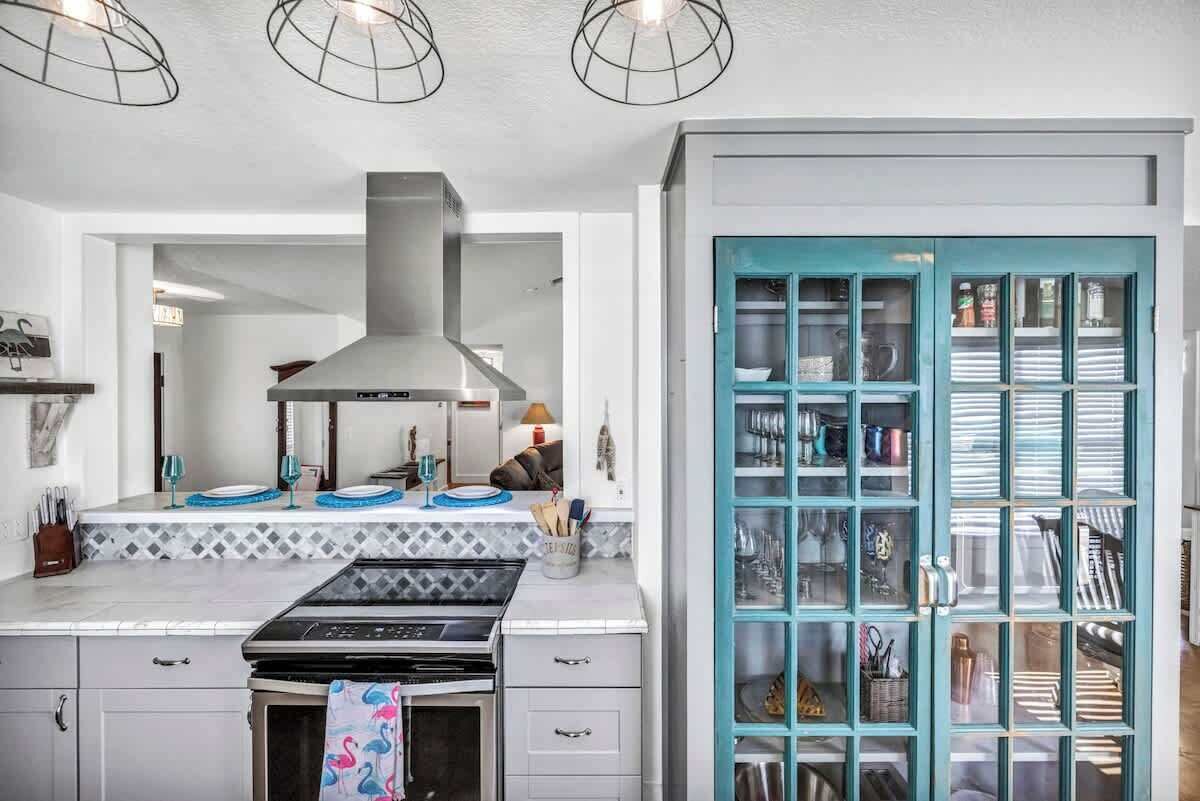 A modern kitchen with a stainless steel range hood, white cabinets, and a teal-colored cabinet with glass doors.