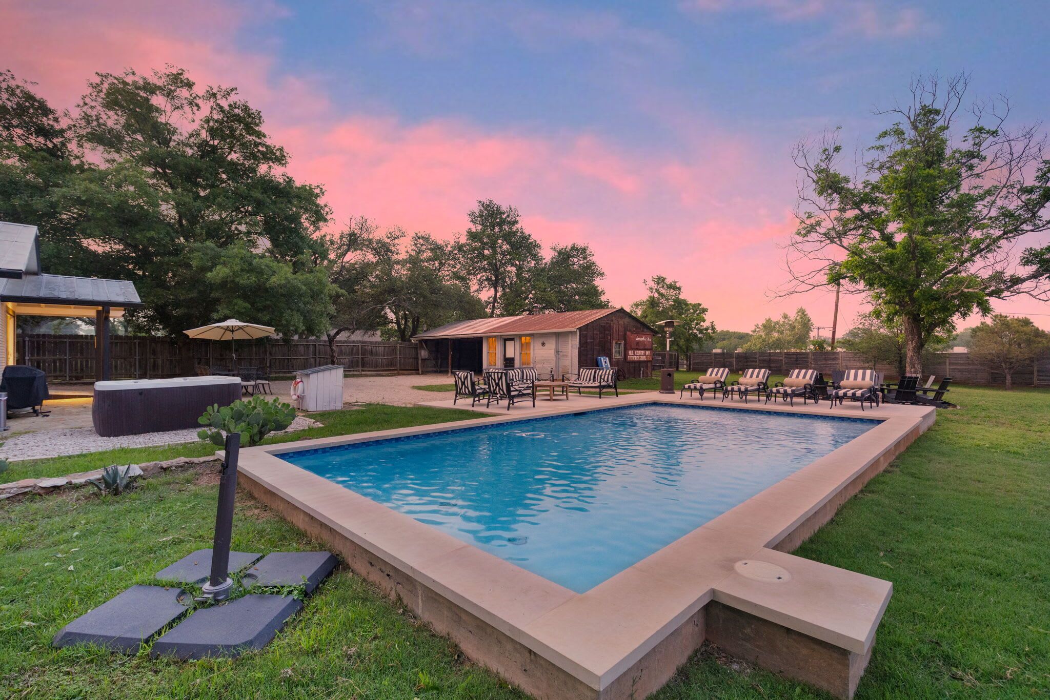 A rectangular swimming pool with a concrete border, surrounded by grass and trees.