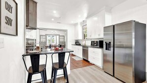 Cocina moderna con armarios blancos, electrodomésticos de acero inoxidable y una barra con dos taburetes.