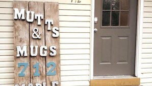 A wooden sign with the text "MUTTS & MUGS 712 MAPLE" against a house exterior.