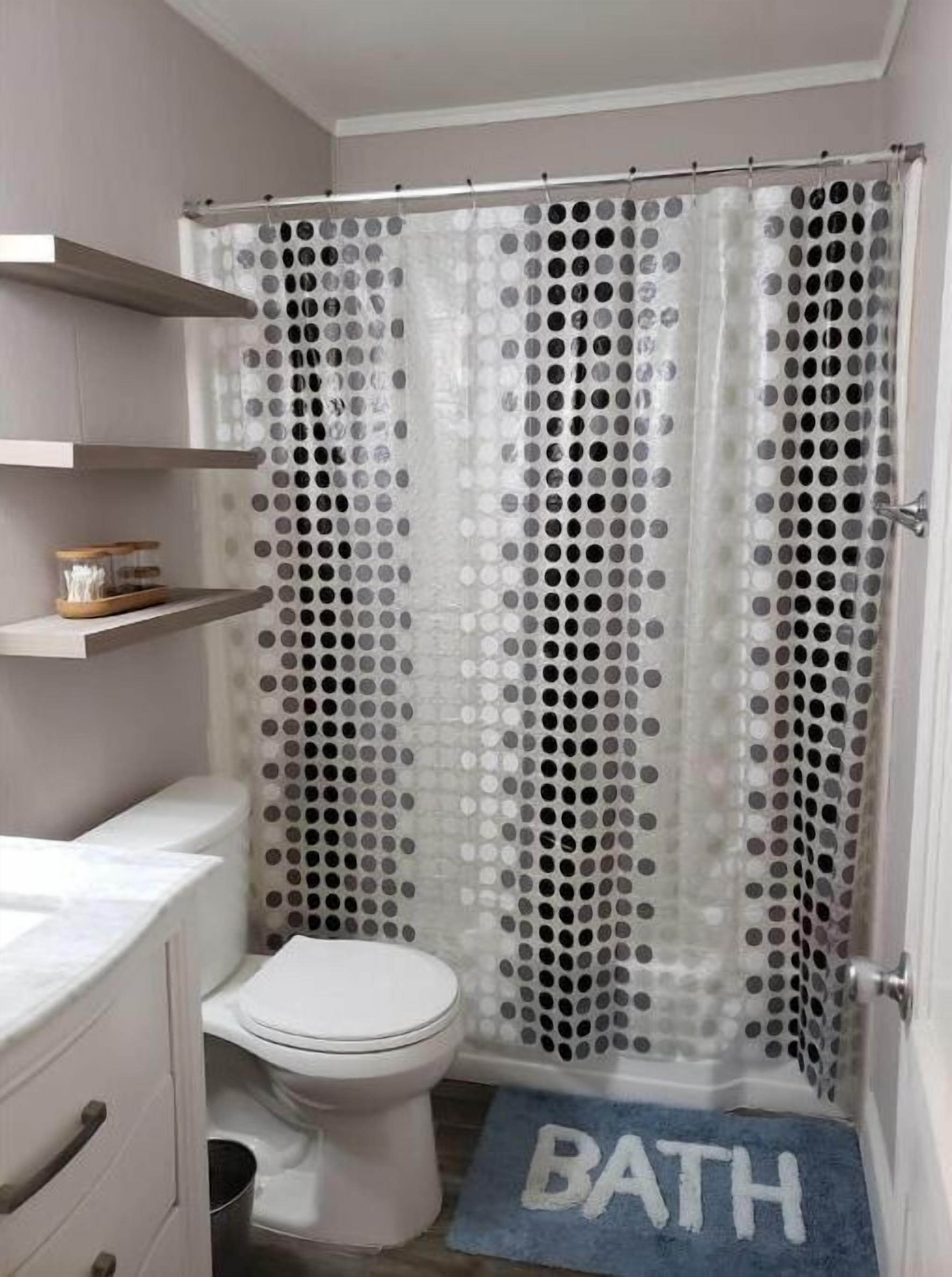 A bathroom with a toilet, a shower curtain with a polka dot pattern, and a blue mat with the word "BATH" on it.