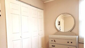 A bedroom with a white wardrobe, a dresser with drawers, and a round mirror.