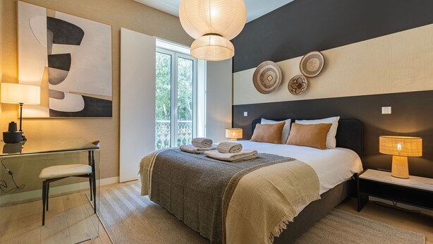 Ein modernes Schlafzimmer mit einem großen Bett, Nachttischlampen, einem Schreibtisch und Blick ins Freie.