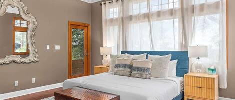 A bedroom with a bed, nightstands, a mirror, and a window with curtains.