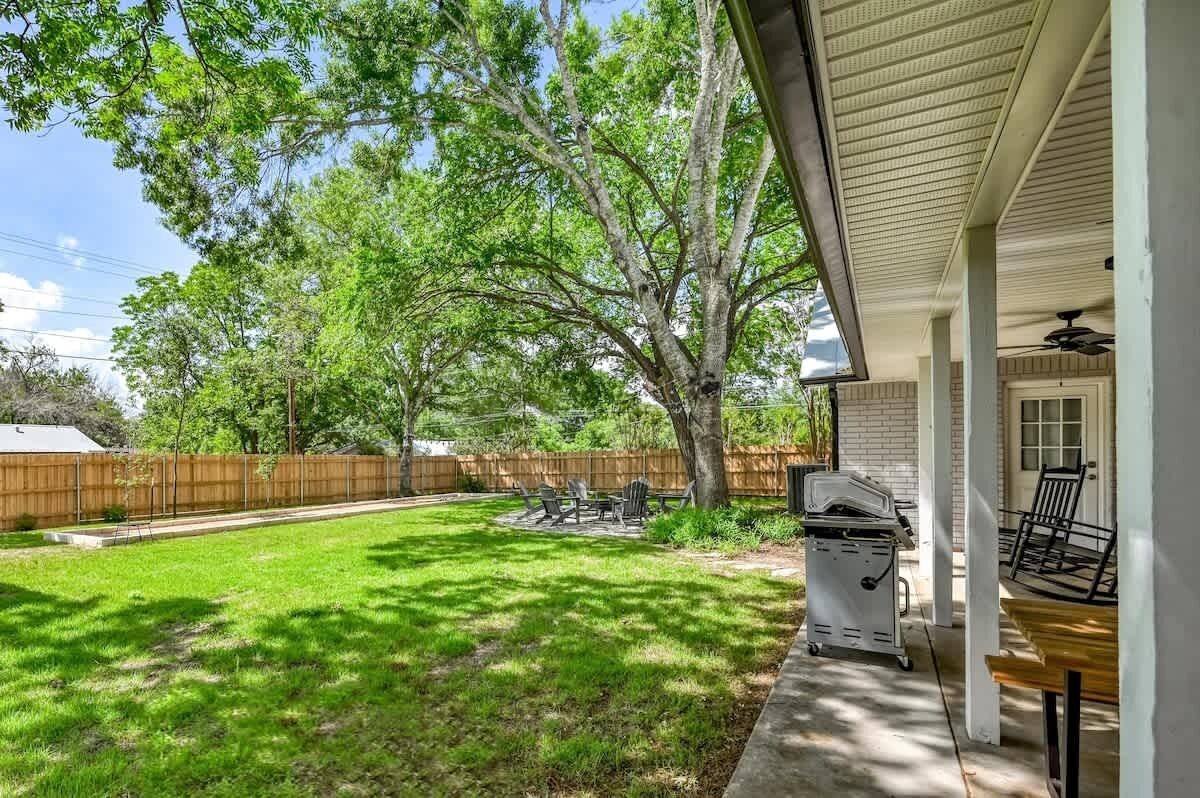 A backyard with a grill, a covered patio, and a wooden fence.