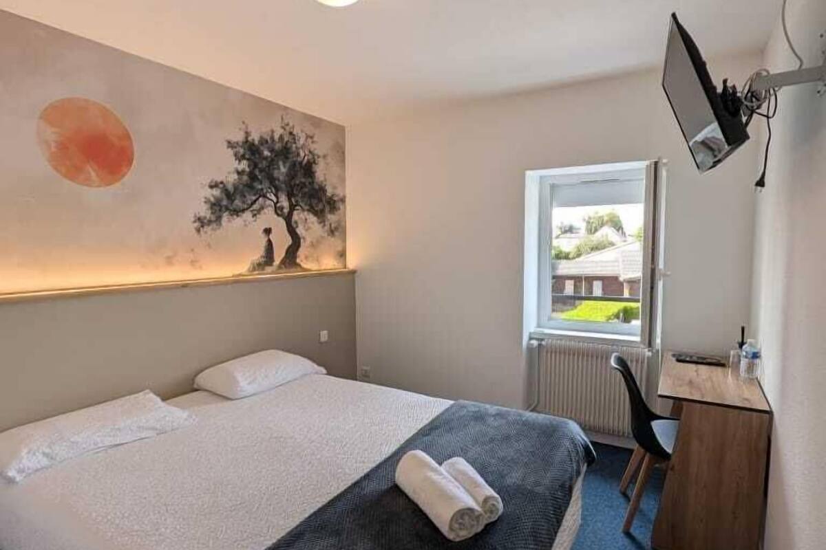 A hotel room with a bed, a desk, a chair, a painting on the wall, and a window.