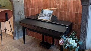Een piano met een lijst met foto, een houten stoel en een vaas met bloemen in een hoek.