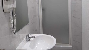 Een badkamer met een witte wastafel, een haardroger en een douchecabine van glas.