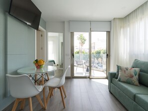 A modern living room with a glass dining table, white chairs, a green sofa, and a TV mounted on the wall. - Zeus By CanariasGetaway (Telde)