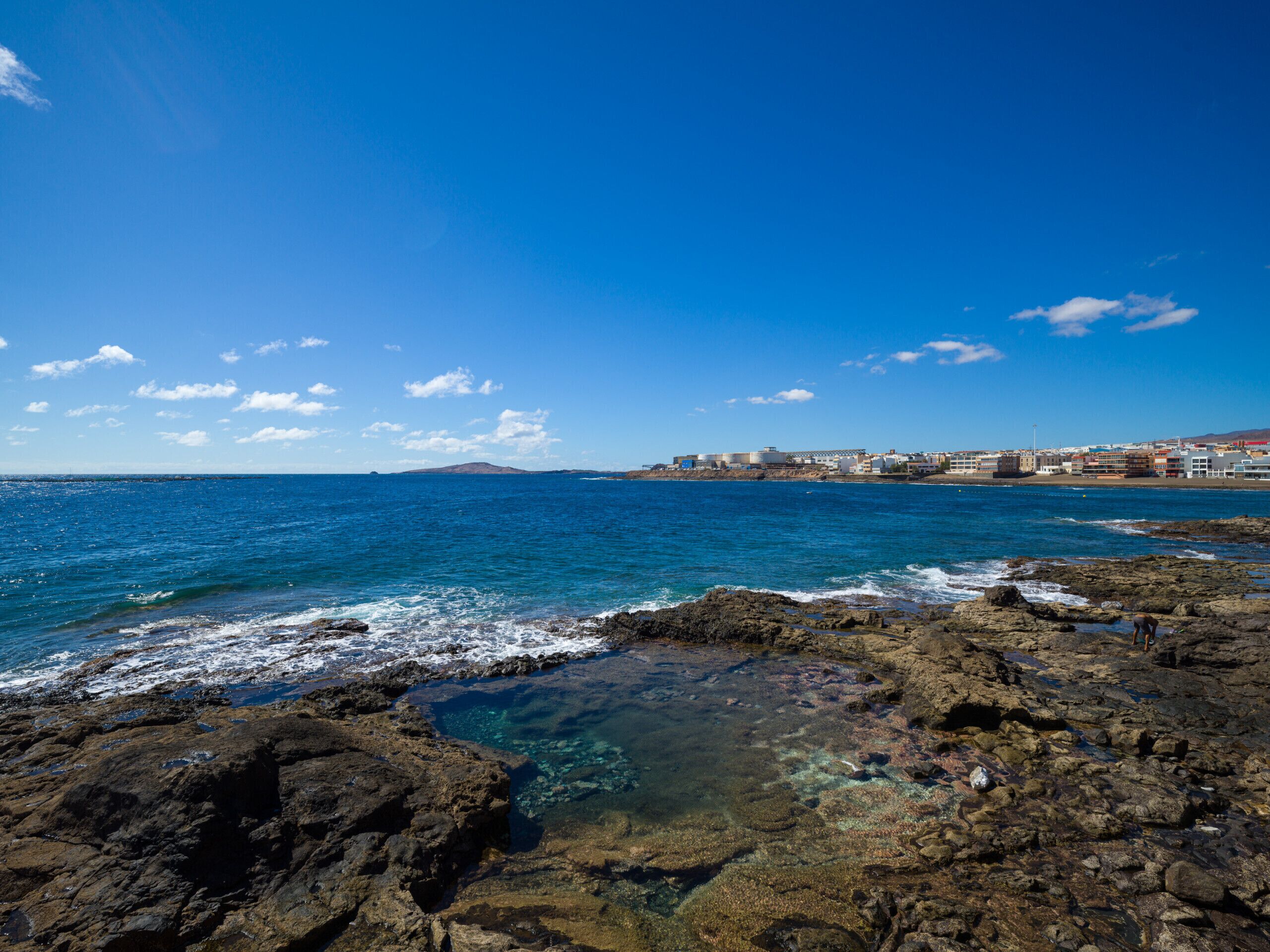 A coastal landscape with rocky shores, clear blue sea, and a distant town.