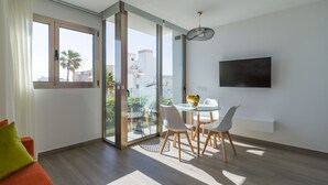 Una sala moderna con un ventanal que da a un balcón, un comedor con mesa y sillas, y un televisor montado en la pared.