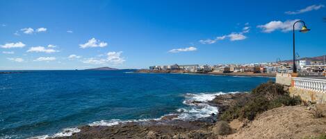 A coastal view with rocky terrain, a clear blue sky, and a distant town with buildings.