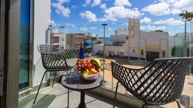 Un balcón con dos sillas, una mesa con frutero y vista a edificios y al cielo.