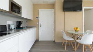 Een moderne keuken met witte kastjes, een koffiezetapparaat en een aan de muur bevestigde televisie.