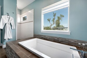 Relax in a spacious bathroom with a large bathtub, shower, and serene views of the surrounding trees.