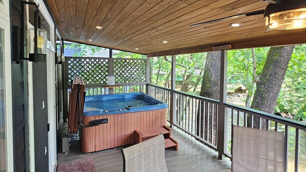 Una terraza techada con un jacuzzi, sillas de madera y una mesa.