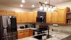 Una cocina moderna con armarios de madera, un refrigerador de acero inoxidable, una isla grande con taburetes e iluminación colgante.