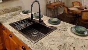 Cocina con encimera de granito, pileta de acero inoxidable, muebles de madera y lámpara colgante.