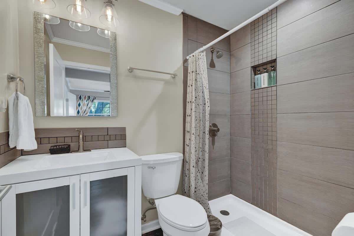 A modern bathroom with a white vanity, a toilet, a shower with a glass door, and a large mirror.